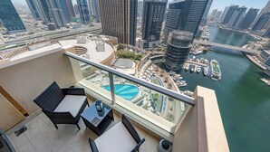 Een balkon met rieten meubilair, uitzicht op een jachthaven en moderne wolkenkrabbers.