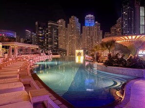 A nighttime view of a hotel pool area with lounge chairs and umbrellas, surrounded by high-rise buildings. - City Meets Sea Elegant Dubai Marina Studio Stay (Dubai)