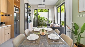 A modern kitchen with built-in appliances, a dining area with a marble table, and a view of a garden through large sliding doors. - Marea Villa by Kozystay - Jimbaran (Jimbaran)