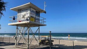 A lifeguard tower with a phone and a flag on top, located on a wooden boardwalk by the ocean.