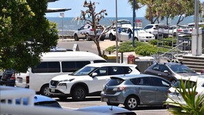 A parking lot with various cars, including a white SUV and a silver hatchback, near a coastal area with a view of the ocean.