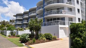A multi-story residential building with balconies, a driveway, and landscaped gardens.
