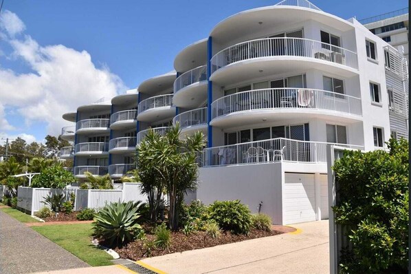 A multi-story residential building with balconies, a driveway, and landscaped gardens.