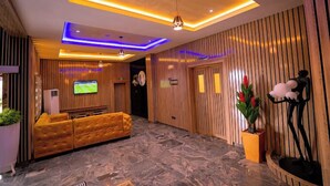 Um hall de entrada com uma mesa de recepção, televisão, sofá e uma planta decorativa.