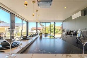 A modern kitchen with a long countertop, overhead lighting, and large windows offering a view of the outdoors. - L'Artbanne - The complete estate (Saint-Hilaire-le-Petit)