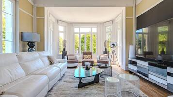 Een moderne woonkamer met een witte bank, een glazen salontafel en een tv op een standaard.