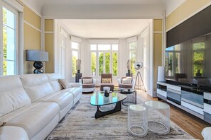 Un salon moderne avec un canapé blanc, une table basse en verre et un téléviseur posé sur un meuble.