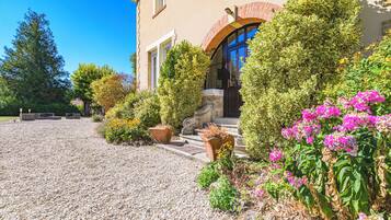 Une maison avec une allée en gravier, un chemin de pierre menant à l’entrée, ainsi qu’une variété d’arbustes et de fleurs.