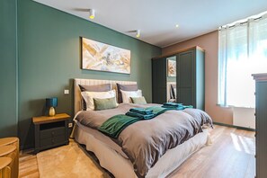 Une chambre à coucher comprenant un lit, une table de chevet, une lampe, un tableau, une armoire et une vue sur l’extérieur.