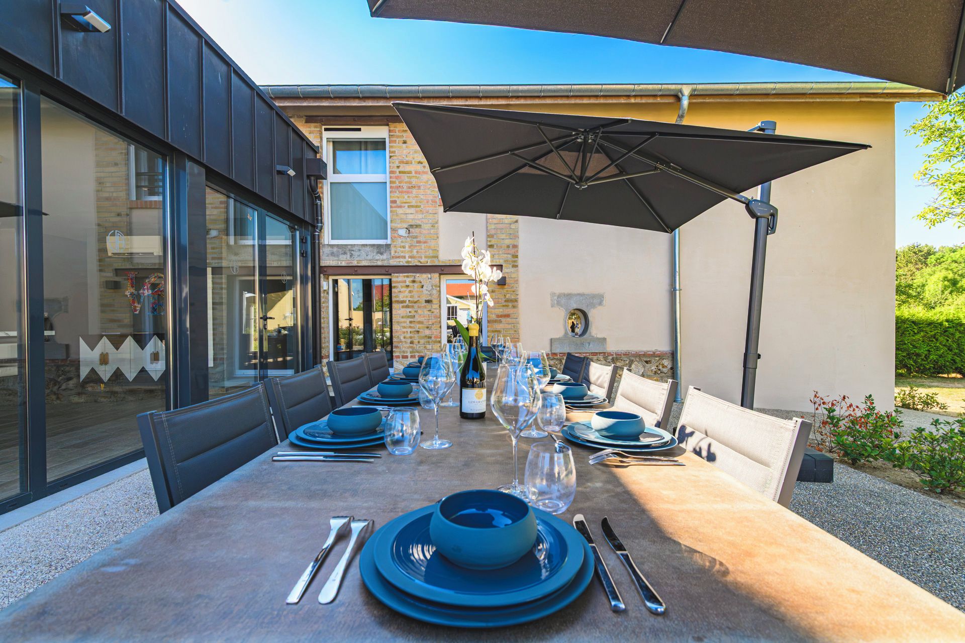 An outdoor dining area with a table set for a meal, surrounded by chairs and an umbrella.