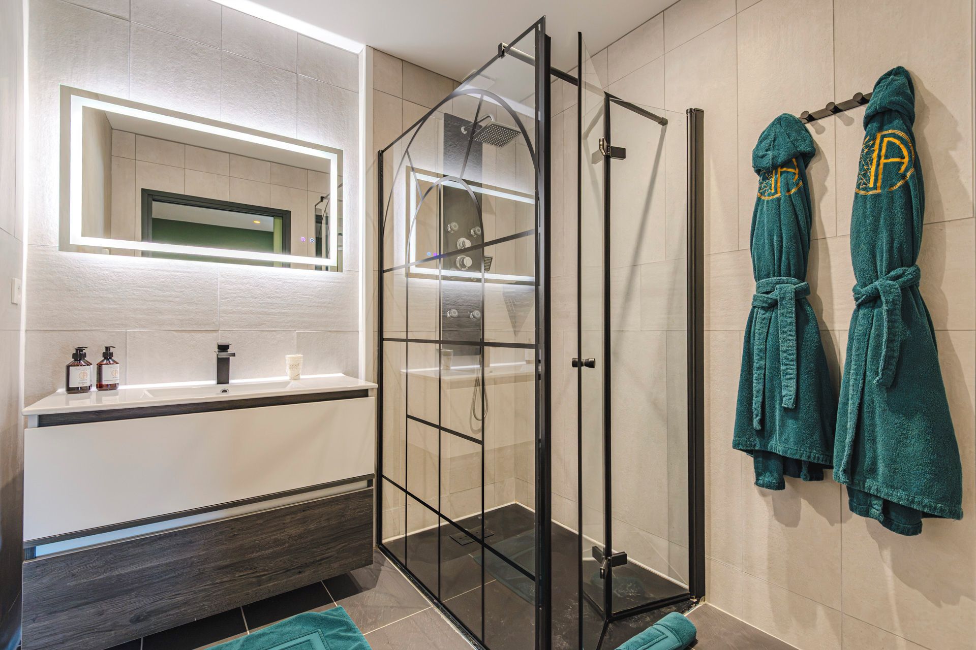 Een moderne badkamer met een douchecabine van glas, een wit wastafelmeubel met een spiegel, en twee blauwgroene handdoeken aan de muur.