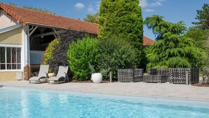 A swimming pool with lounge chairs, a covered patio, and a tiled roof.