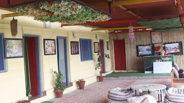 A covered outdoor area with colorful doors, potted plants, and a table with ottomans. - Ooncha Dana Home Stay (Uttarakhand)