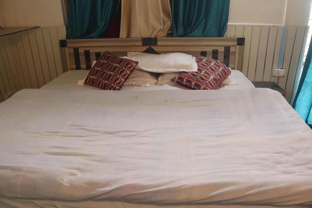 Una cama con ropa blanca, dos almohadas estampadas, un cabecero de madera y cortinas color turquesa.