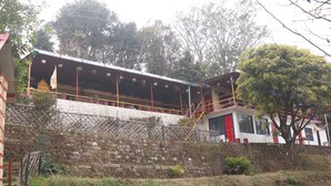 A building with a balcony, a red door, and a stone wall. - Ooncha Dana Home Stay (Uttarakhand)
