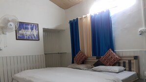 A bedroom with a bed, a fan, a picture on the wall, and curtains. - Ooncha Dana Home Stay (Uttarakhand)