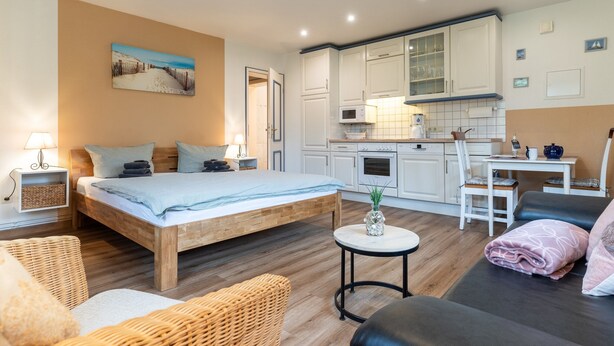 Ein Schlafzimmer mit Bett, Nachttischen, einem kleinen runden Tisch, einer Couch und einer Küchenzeile mit Schränken und Geräten.