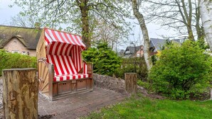 Ein Strandkorb mit gestreiftem Sonnensegel in einem Garten.