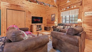 Ein gemütliches Blockhaus-Interieur mit einem Holz-Fernsehschrank, zwei braunen Sofas, einem Couchtisch und einem Fenster mit Aussicht.