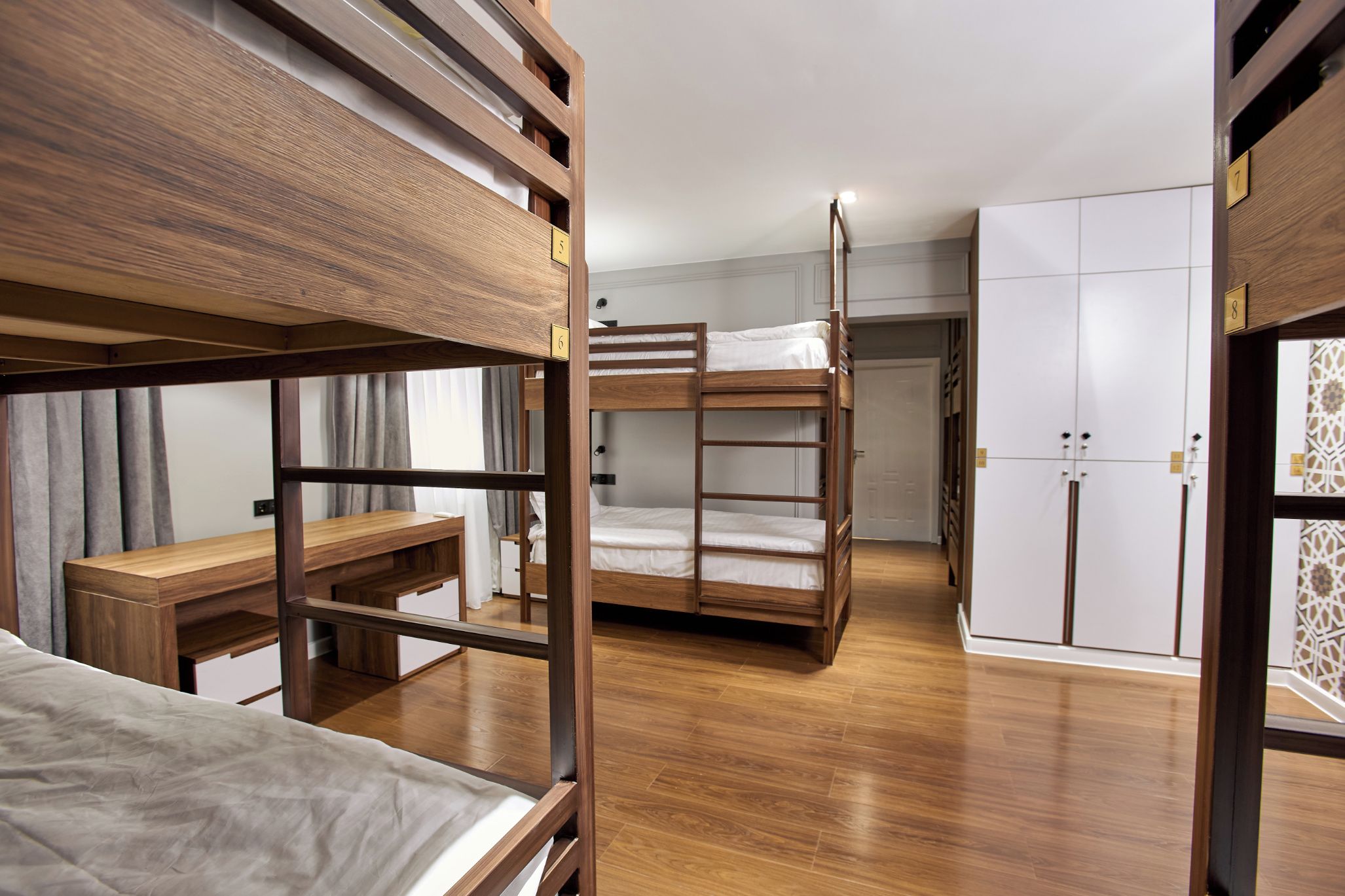 A bunk bed room with a wooden desk and wardrobe.