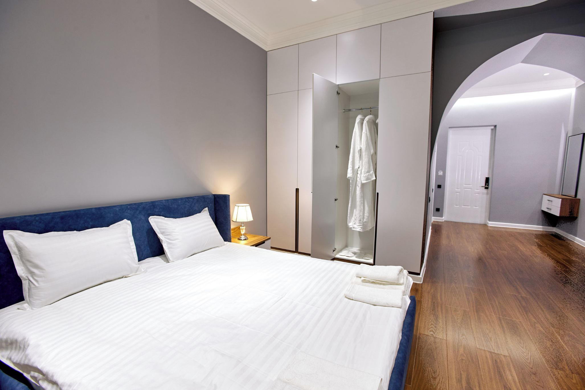 A hotel room with a large bed, a wardrobe, a mirror, and a door leading to another room.