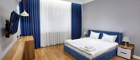 Una habitación de hotel moderna con una cama grande, un escritorio de madera, una mesita de noche y un televisor fijado a la pared.