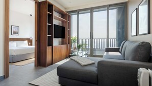Un salon moderne avec un canapé gris, un téléviseur à écran plat et un balcon doté d’une porte vitrée.