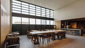 Une pièce spacieuse avec une grande table et des chaises, un coin bar avec des tabourets et de grandes fenêtres donnant sur les bâtiments environnants.