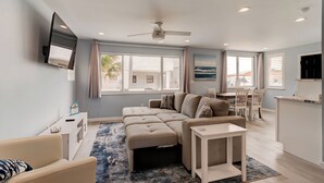A modern living room with a sectional sofa, a small table, and a TV mounted on the wall. - The Turtle Nest - Steps to the Sand! 
 (Ormond Beach)