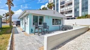 A small, light blue building with a covered patio area, numbered 13, adjacent to a modern high-rise building. - The Turtle Nest - Steps to the Sand! 
 (Ormond Beach)