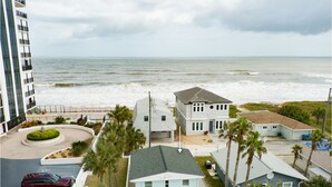 A coastal residential area with a view of the ocean, featuring houses with a mix of architectural styles, a parking area, and a landscaped garden. - The Turtle Nest - Steps to the Sand! 
 (Ormond Beach)