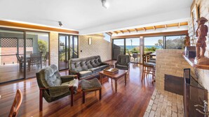 A spacious living area with a fireplace, a sofa, and a coffee table. - Caloundra Retro Beach House in Front of Ocean (Caloundra Region)