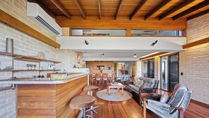 A modern kitchen with a bar area, wooden flooring, and a loft dining space. - Caloundra Retro Beach House in Front of Ocean (Caloundra Region)