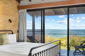 A bedroom with a large sliding glass door leading to a balcony with a view of the ocean.