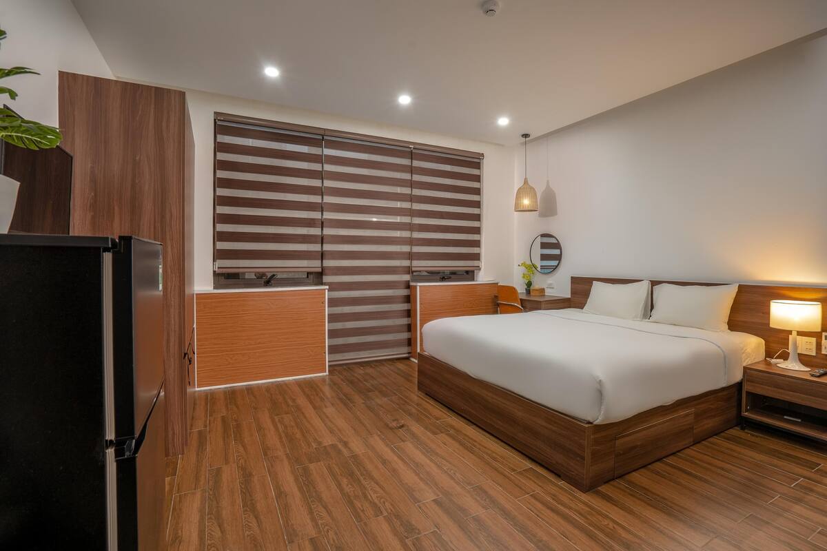 Habitació d'hotel moderna amb sòl de fusta, un llit gran, una taula de nit, un escriptori i un armari amb portes corredisses.