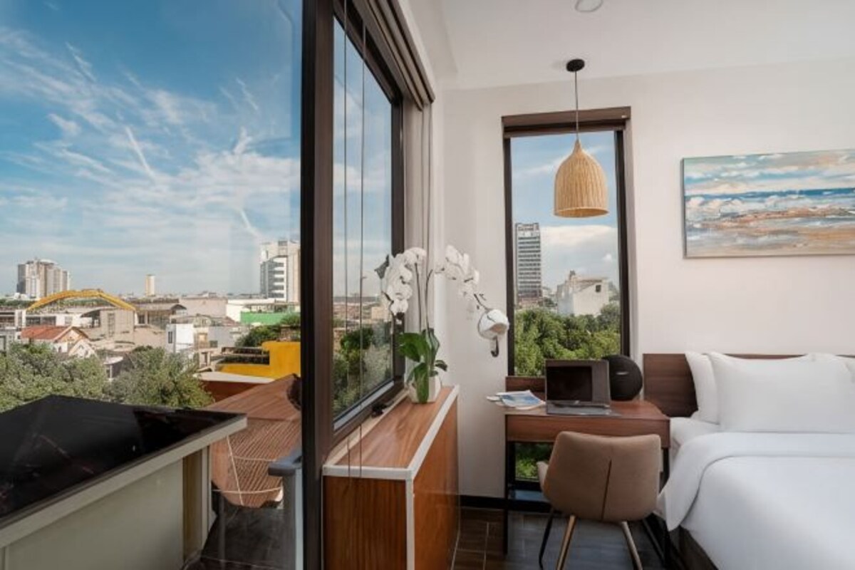 A modern hotel room with a city view, a dining area, and a bed.