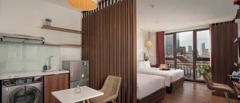 A hotel room with a bed, a desk, a chair, a washing machine, and a view of the city.