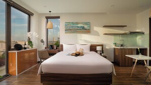 A modern hotel room with a large bed, a desk, a small kitchenette, and a large window offering a city view. - Dragon View Riverfront Hotel  (Da Nang)