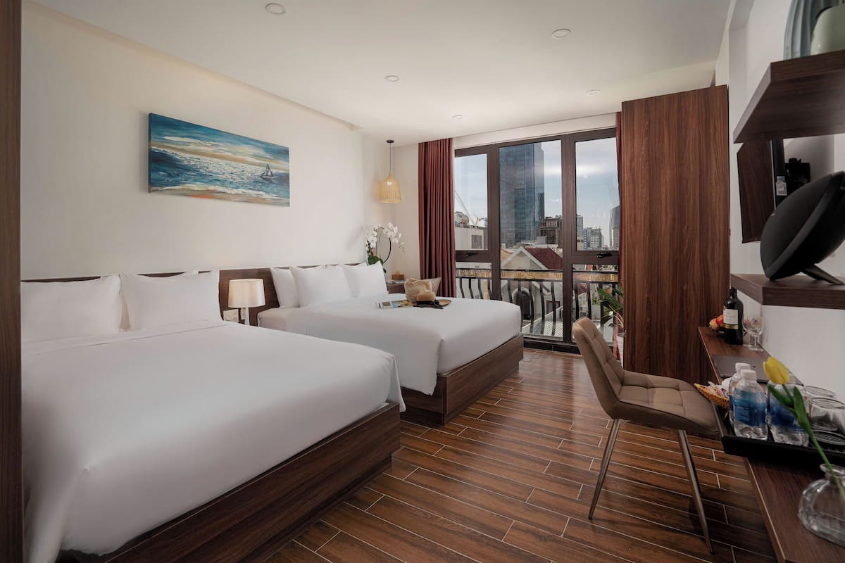 Una habitació d'hotel amb dos llits, una taula, una cadira, un televisor i una finestra gran amb vista a la ciutat.