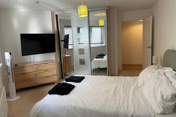 A bedroom with a bed, a TV, a dresser, and a mirror.