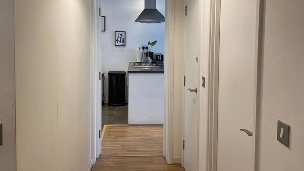 Un pasillo con piso de madera que conduce a una cocina con estufa moderna y una lámpara colgante.