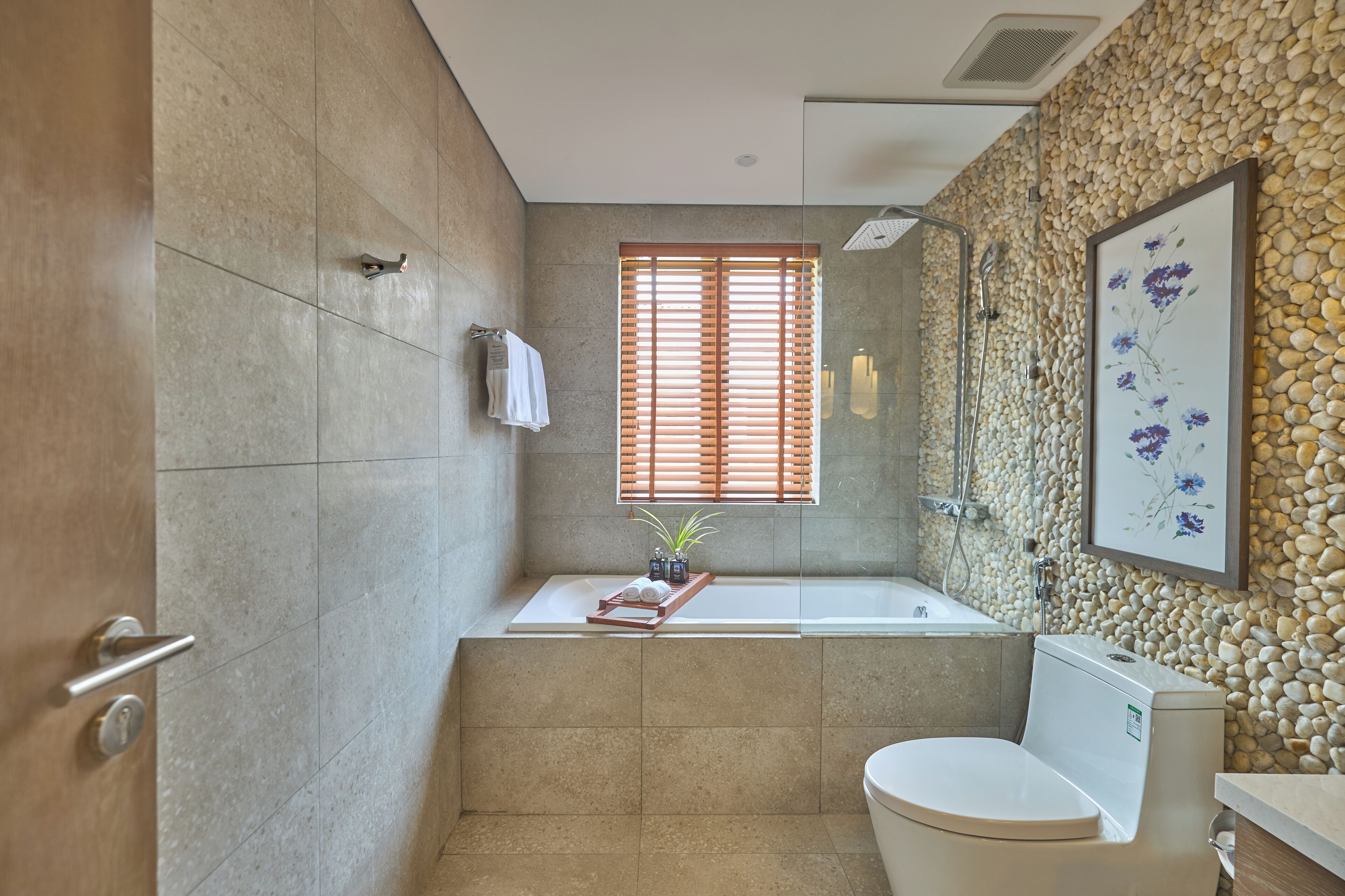 Un baño moderno con bañera, inodoro y ventana con persianas de madera.