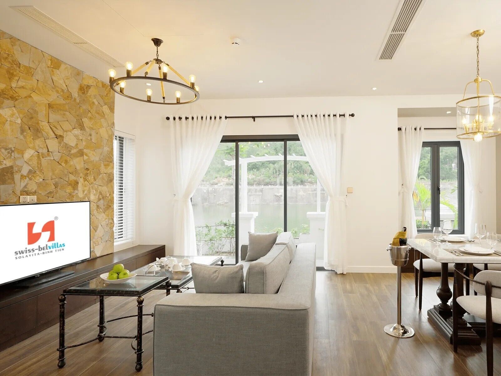 A modern living room with a stone wall, a sofa, a dining table set for two, and a TV displaying a logo.