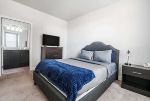 A bedroom with a bed, a TV, a nightstand, a dresser, and a mirror.