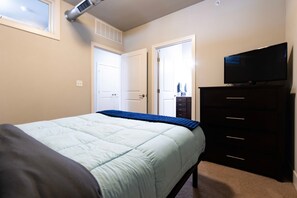 A bedroom with a bed, a dresser, a television, and a window.