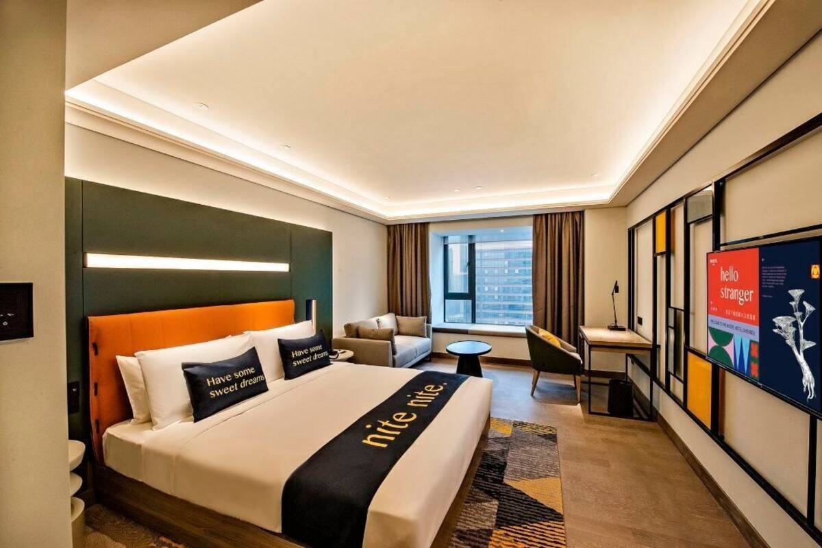 Ein modernes Hotelzimmer mit einem großen Bett, einem Schreibtisch, einem Sessel und Blick auf die Stadt.