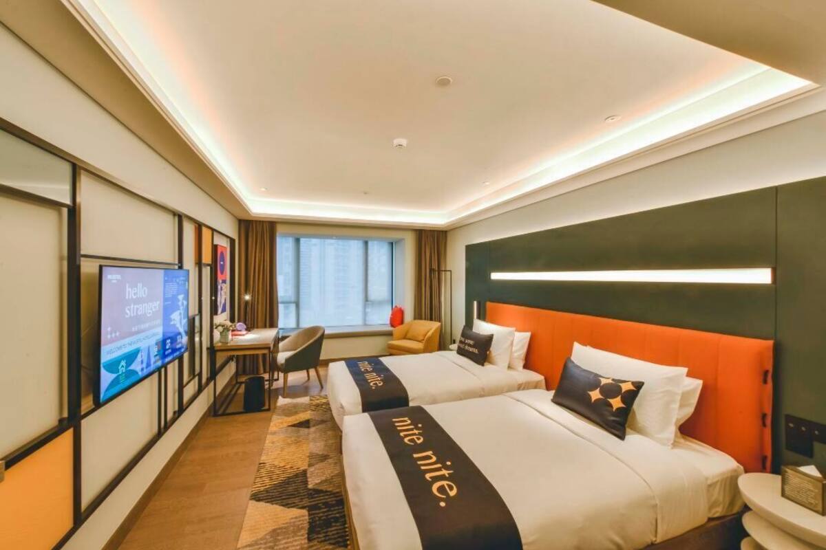 Ein Hotelzimmer mit zwei Betten, einem Schreibtisch, einem Stuhl, einem Fernseher und einem Vorhangfenster.
