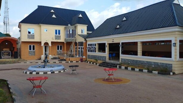 A building with a covered outdoor area, a fountain, and outdoor seating. - Solid Worth Hotels (Ilorin)