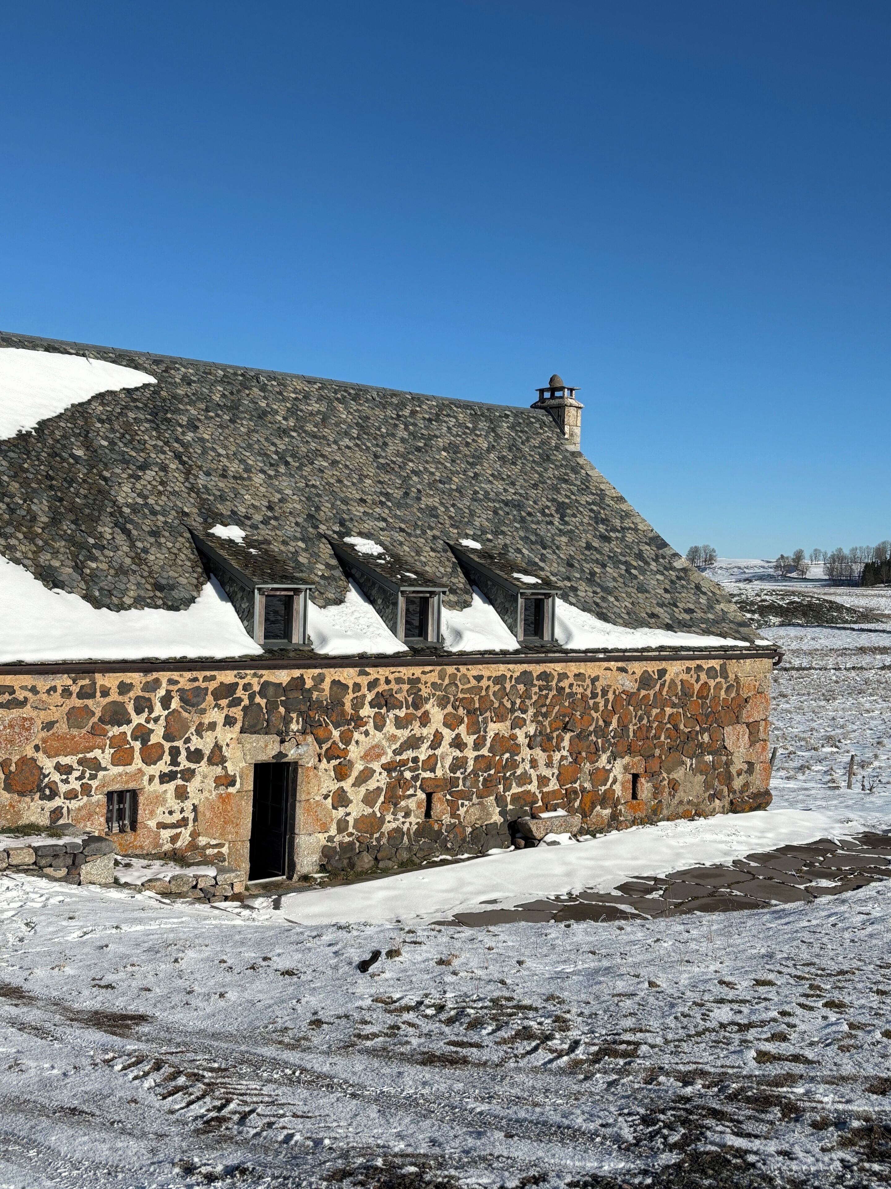 A stone building with a sloped roof and a chimney, surrounded by snow.