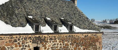 A stone building with a sloped roof and a chimney, surrounded by snow.